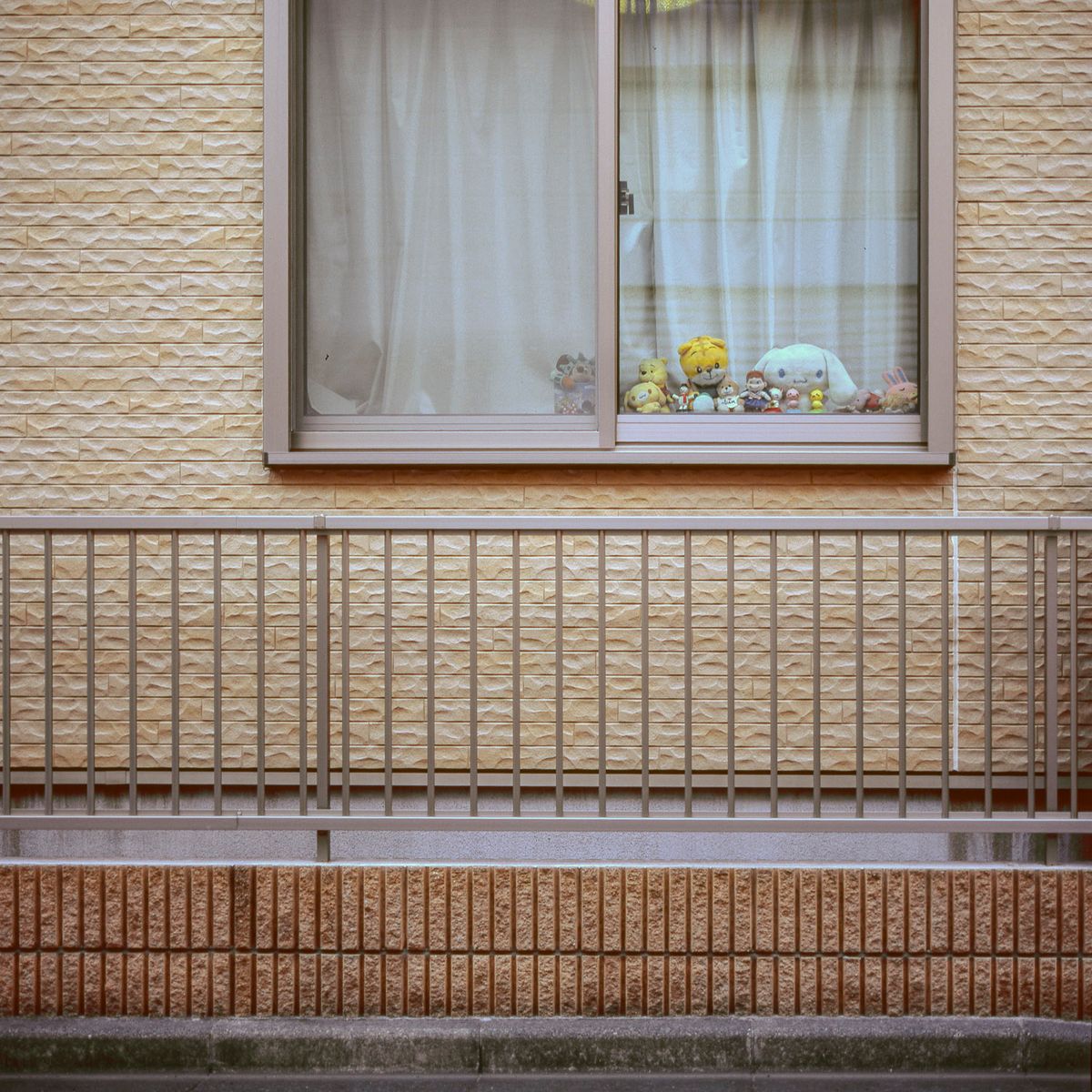 Ventana con cortinas blancas y pequeñas figuras en el alféizar, sobre una fachada de azulejos beige