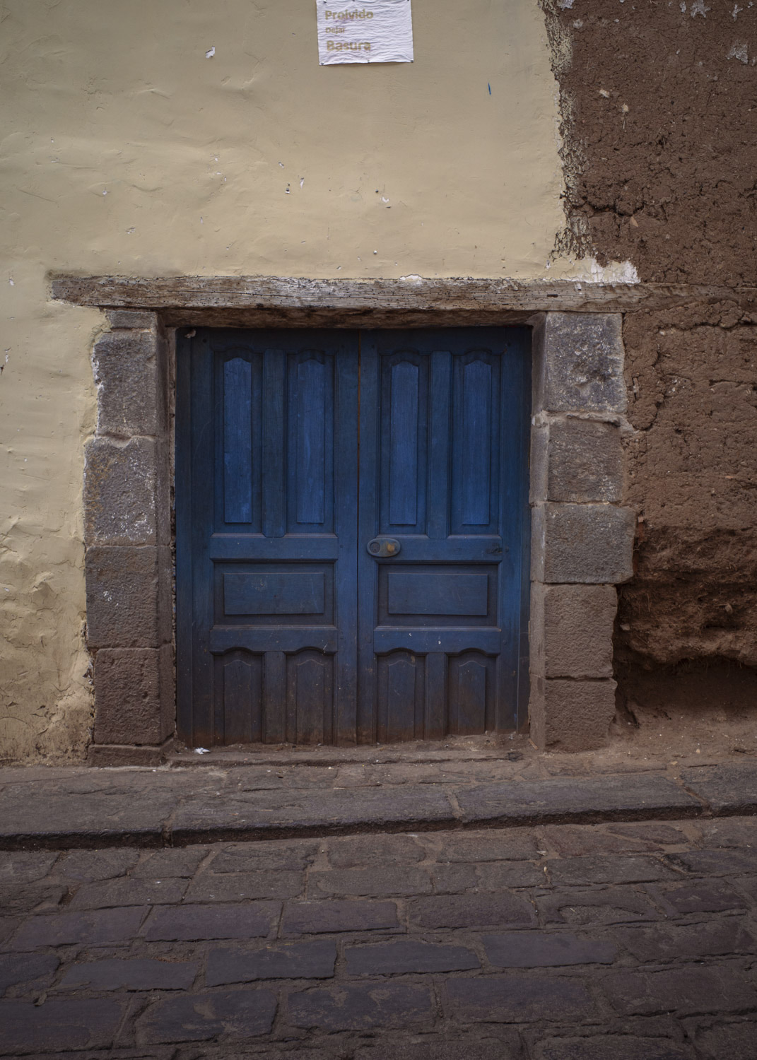 Puerta doble azul baja, enmarcada por piedras bajo una pared de yeso.