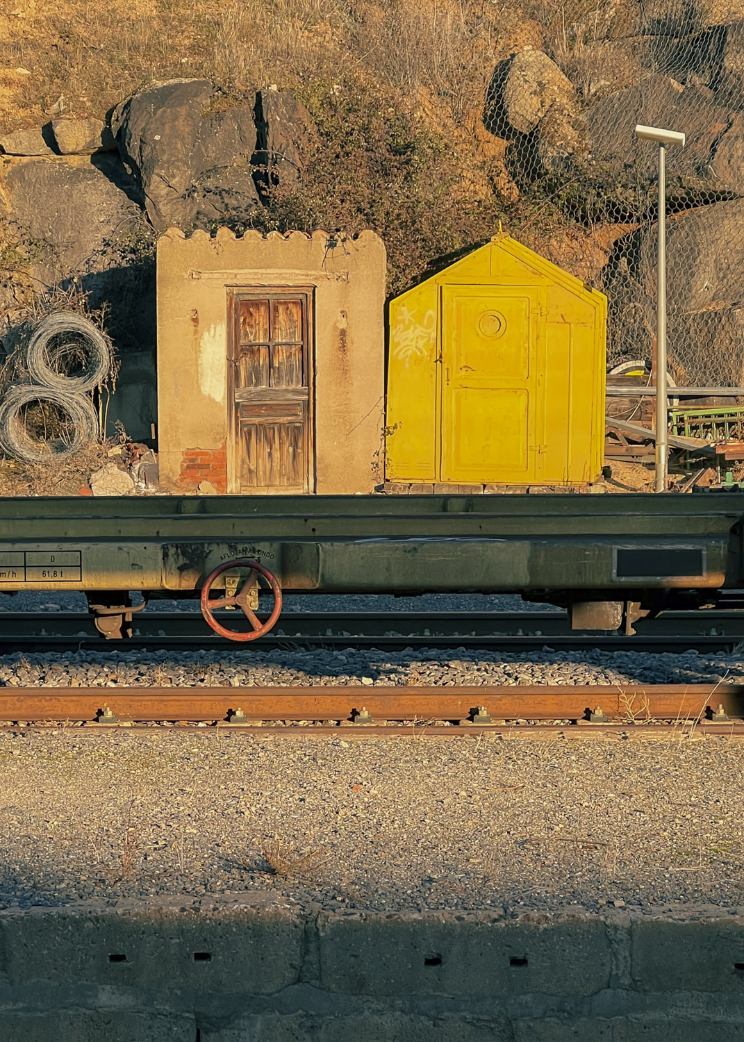 Dos pequeñas casetas, una amarilla, sobre un vagón plano junto a vías de tren.