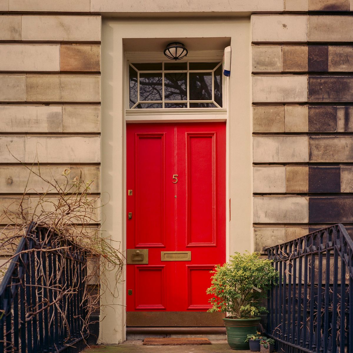 Puerta roja con el número 5 y vidriera superior, entre barandillas negras.