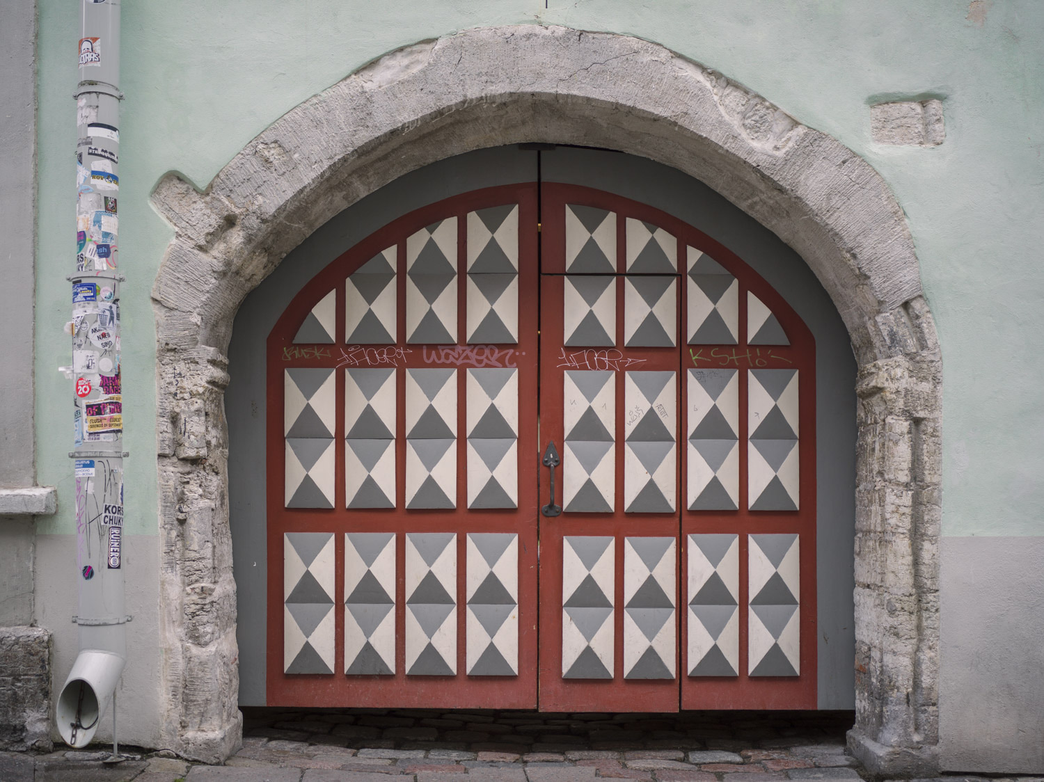 Portón rojo de arco apuntado con paneles de rombos blancos, grises y negros.