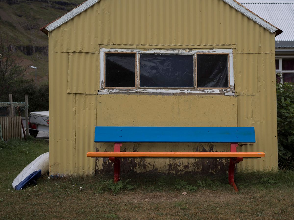 Banco de colores frente a una caseta amarilla con una ventana horizontal.