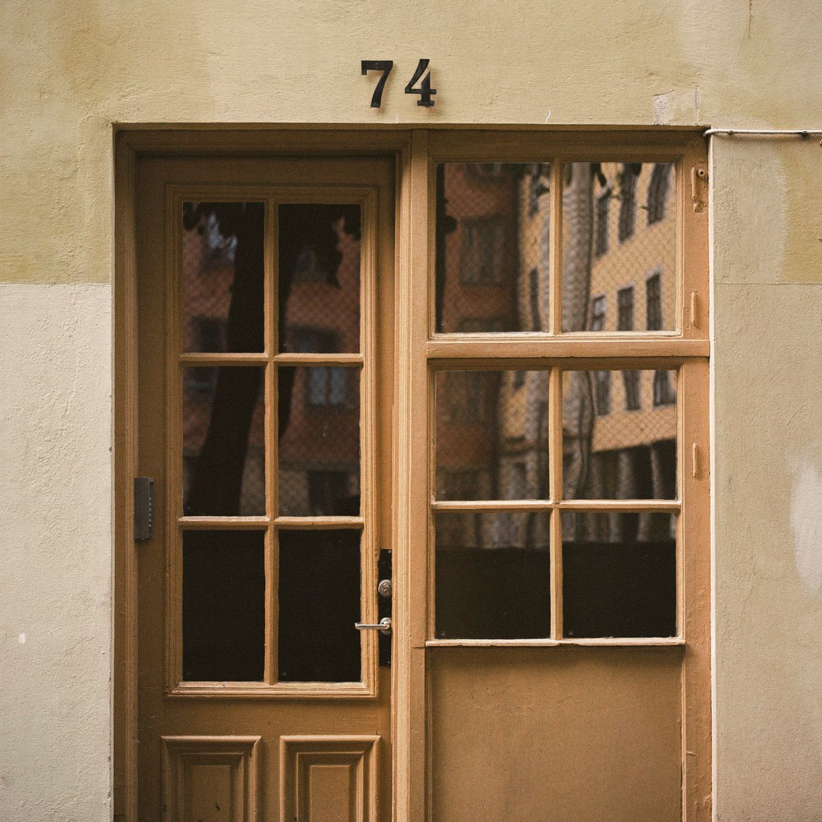 Puerta acristalada y ventana reflejando edificios, bajo el número 74.