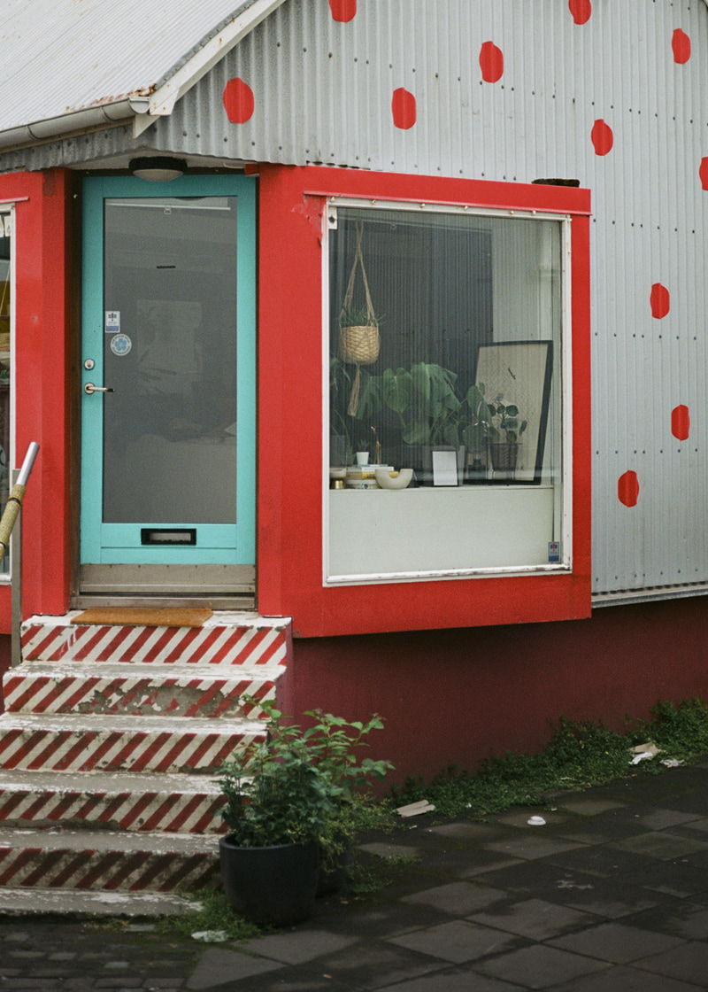 Fachada blanca con lunares rojos, puerta turquesa y escaparate con marco rojo.