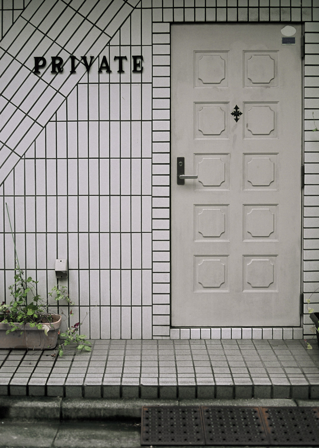 Puerta blanca cerrada en una fachada de azulejos blancos, junto a la palabra «PRIVATE».