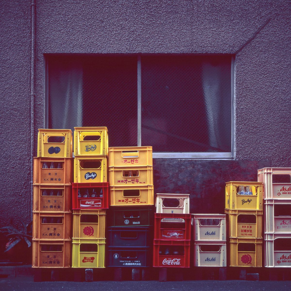 Pilas de cajas de bebidas amarillas y rojas delante de una ventana.