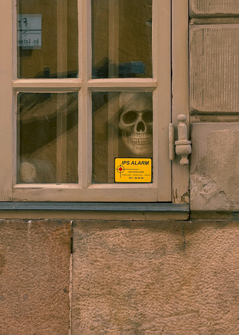 Calavera visible detrás de una ventana de madera junto a una pegatina amarilla de alarma.