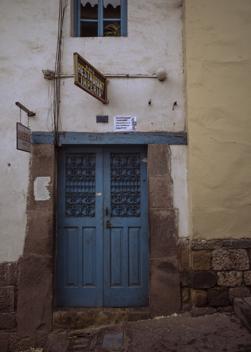 Puerta doble azul con rejas ornamentales, entre paredes blancas y piedras expuestas.